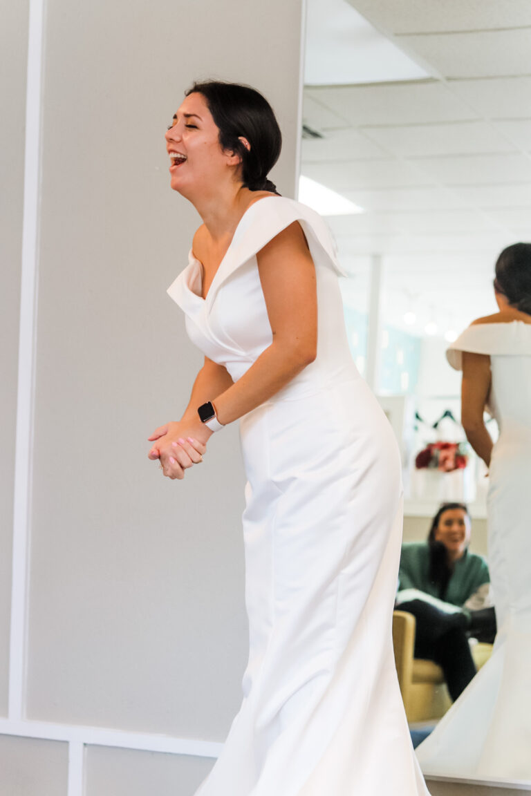 Ecstatic bride laughing in off-shoulder wedding gown during joyful dress fitting in Austin bridal boutique with Olive & Eden Weddings