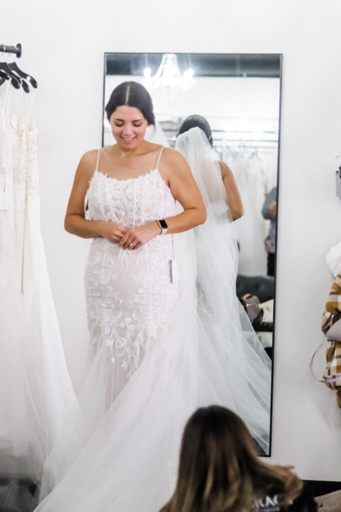 Joyful bride in intricate lace wedding gown and veil during fitting adjustment in Austin boutique with Olive & Eden Weddings