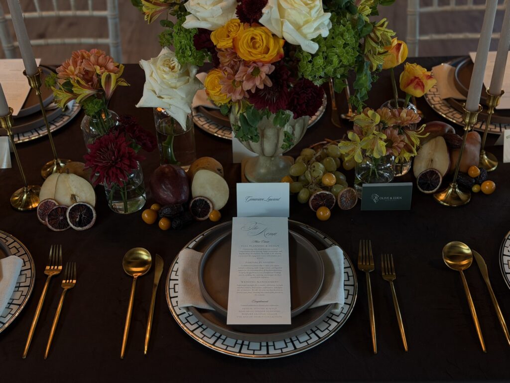 Landscape view of luxury wedding tabletop decor featuring gold flatware, matte brown stoneware, and abundant fruit styling by Austin wedding planner Olive & Eden.