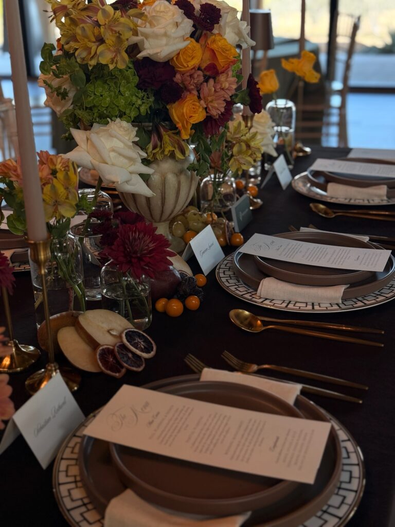 Angled close-up of a Dutch Masters inspired wedding centerpiece featuring mustard roses, deep burgundy mums, and sliced fruit accents styling by Austin wedding planner Olive & Eden.