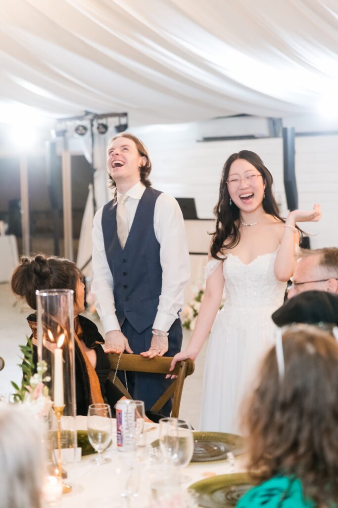 Candid photography of a bride and groom laughing during toasts at their intimate garden wedding reception.