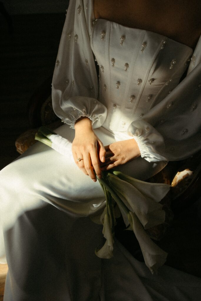 A cinematic detail shot of a wedding dress focusing on light, shadow, and tactile texture.