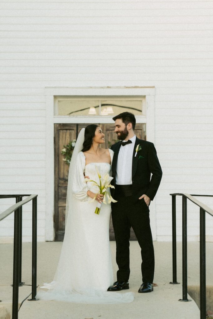 A timeless wedding portrait of a couple standing in front of the historic white doors of Hill Country Wedding Chapel