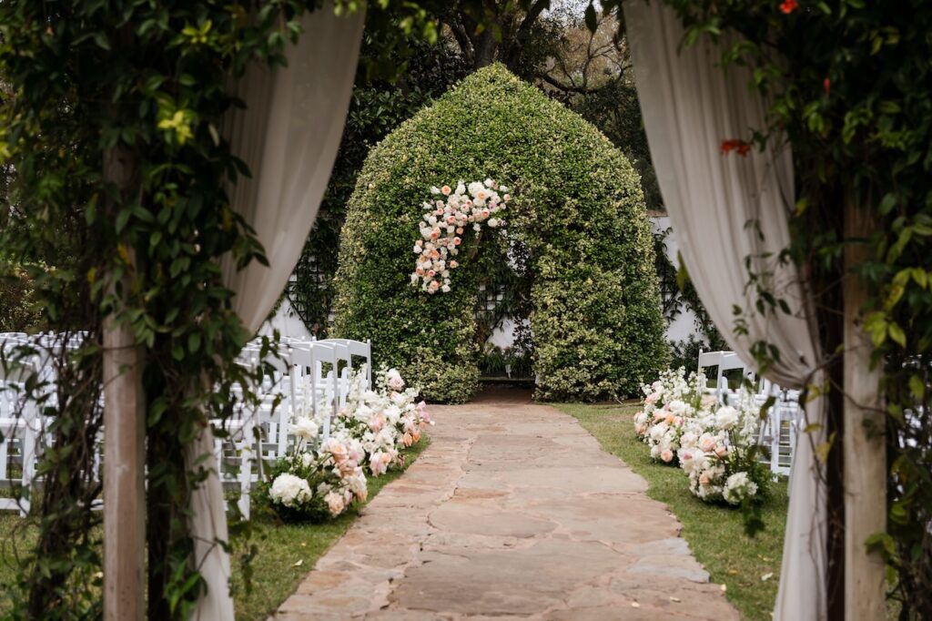 A lush floral ceremony arch nestled in the gardens of Hummingbird House, designed by Austin wedding planner Olive & Eden.