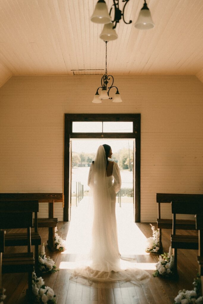 A cinematic silhouette of a bride standing in the light of the historic Hill Country Wedding Chapel doorway in Fredericksburg, Texas.