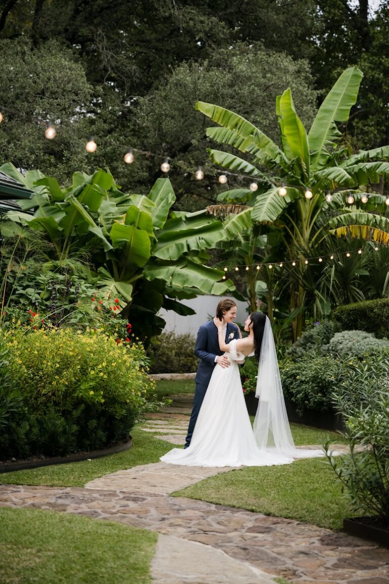 A romantic garden wedding portrait at Hummingbird House designed by Austin wedding planner Olive & Eden, featuring a bride and groom on a stone path under bistro lights.