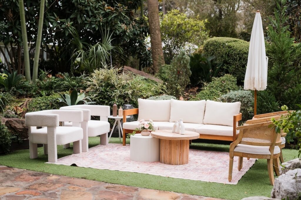 A high-end outdoor wedding lounge featuring neutral velvet furniture and curated floral arrangements for an intimate garden reception.