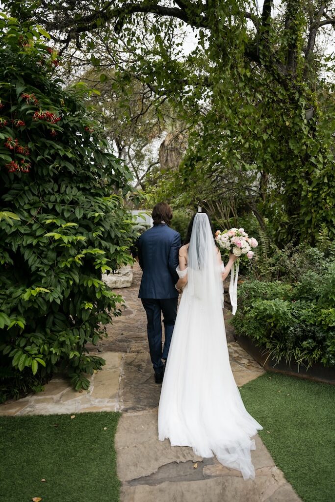 A romantic back-view portrait of a bride and groom walking along the signature stone path at a Hummingbird House garden wedding.